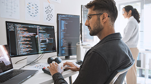 Data science professional analyzing code and data structures on multiple monitors in a modern office setting